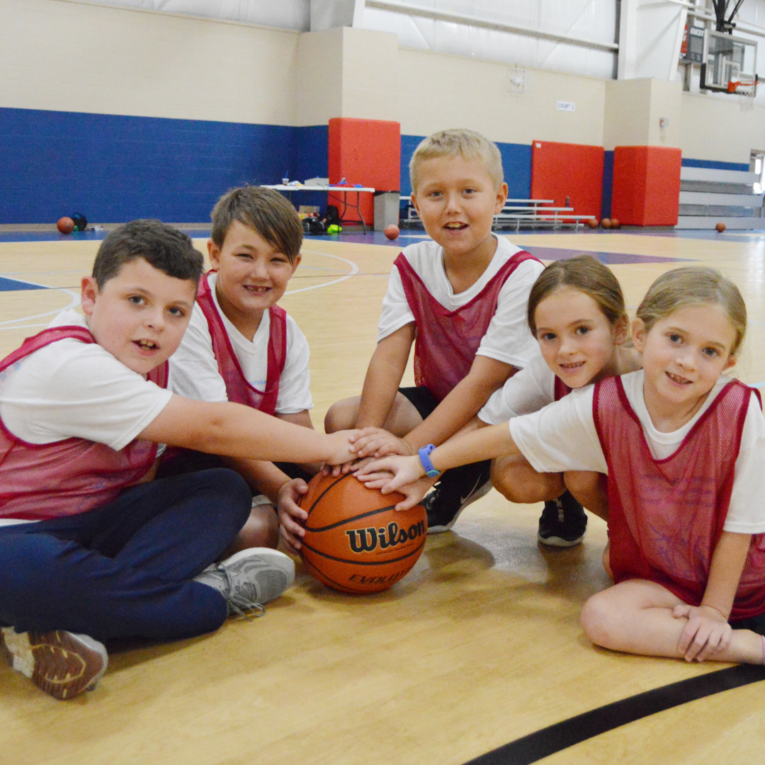 five kids in a group with one hand on the basketball in the middle